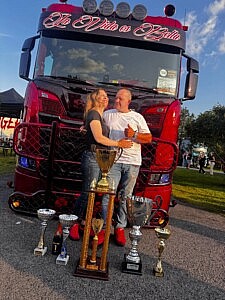Frau heinrichs und Sascha Heinrichs vor Ihrem Hängerzug la Vida es Bella mit den gewonnen Pokalen von der Power truck Show in finnland 2025. darunter zum dritten mal als Best of Show gekürt